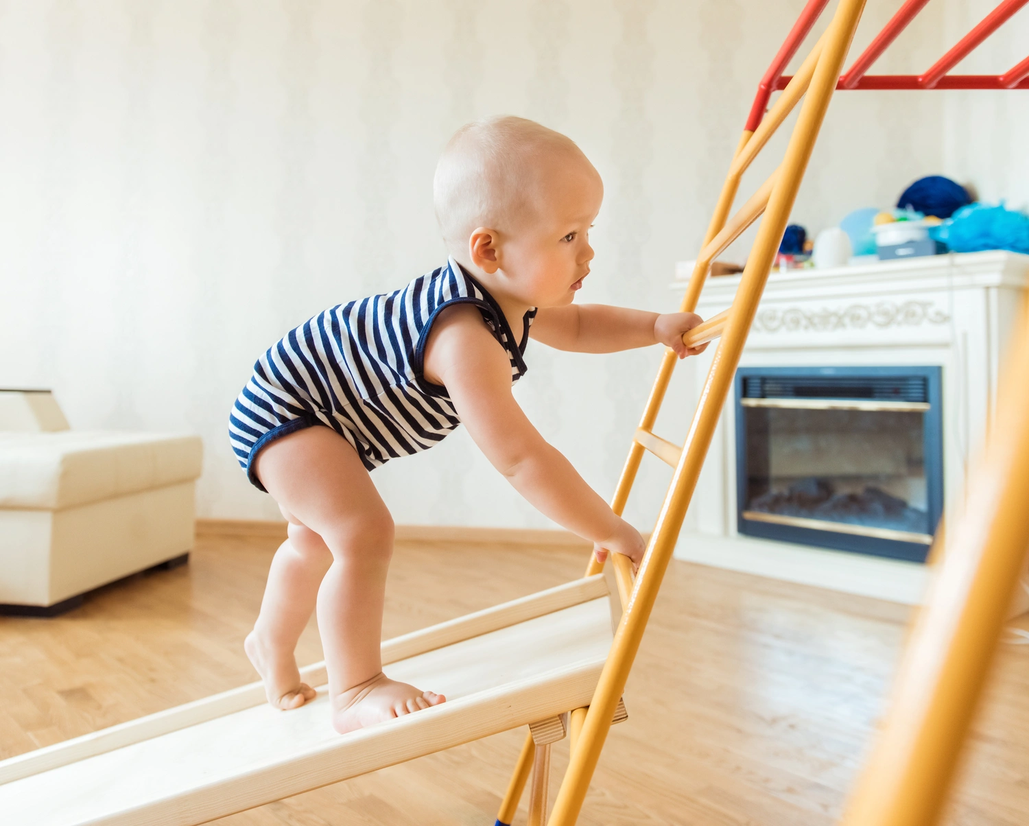 Cute baby performs gymnastic exercises on a wooden home sports complex stairs and rings